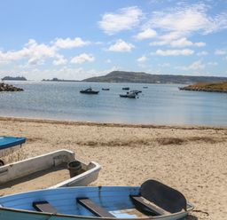 A sandy beach with small boats on the shore and boats floating on water at Sandpiper in Weymouth