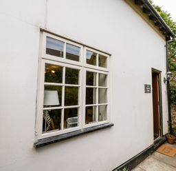 Exterior side wall of a white cottage with a window and an open door showing a welcome mat at Hock-tide Cottage in Kenilworth