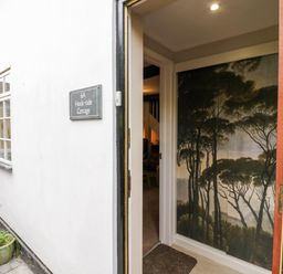 An open door showing the entrance with a wall mural of trees inside at Hock-tide Cottage in Kenilworth