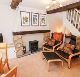 A sitting area with chairs a small stove and dining table near stairs at Hock-tide Cottage in Kenilworth