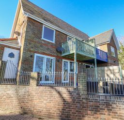 The exterior of a two-story brick house with balconies and metal fencing at Castle Cove Cottage in Weymouth
