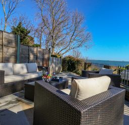 An outdoor patio with wicker seating and a table overlooking the sea at Castle Cove Cottage in Weymouth
