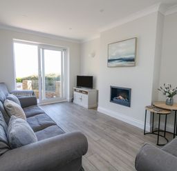 A living room with two grey sofas a small table with flowers a wall mounted fireplace and a tv on a cabinet at Castle Cove Cottage in Weymouth