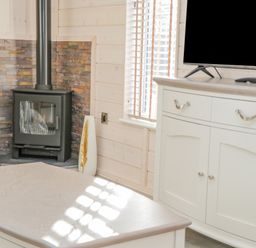 A corner with a black wood burning stove surrounded by stone tiles next to a window and a white cabinet with a TV on top at No 27 The Crab Pot in Runswick Bay near Staithes