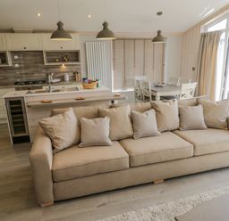 A living room with a beige sofa and an open kitchen with dining table and chairs at No 27 The Crab Pot in Runswick Bay near Staithes