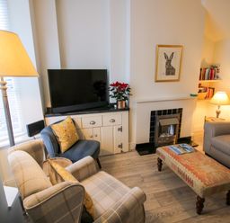 A living room with a TV on a cabinet a fireplace armchairs and a sofa at Primrose Cottage in Winchcombe