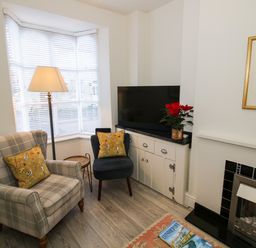 A sitting area with two armchairs a floor lamp a cabinet with a television and a fireplace at Primrose Cottage Winchcombe