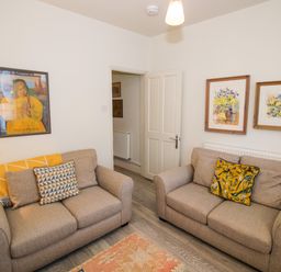 A room with two beige sofas with patterned cushions a framed poster and two floral paintings on the walls at Primrose Cottage in Winchcombe