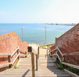 A wooden staircase with railings between brick walls leading down to a waterfront at Blanche Cottage Brewers Quay Harbour