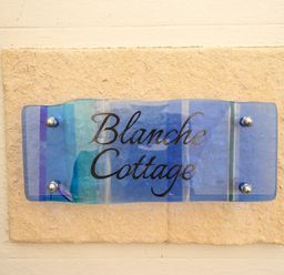 A blue glass sign with the text Blanche Cottage mounted on a stone slab on a wall at Blanche Cottage Brewers Quay Harbour