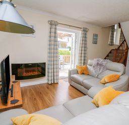 A living room with grey sofas and orange cushions next to a wall-mounted electric fireplace and a television at Oak Tree Cottage in Aberporth