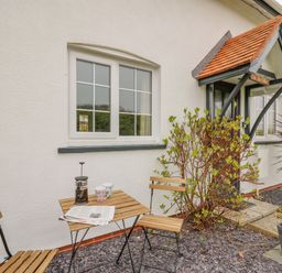 A small outdoor seating area with a wooden table and two chairs outside a white house at Oak Tree Cottage in Aberporth