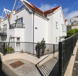 A row of white houses with red roofs and black railings next to a parking area at Puffins in Tenby