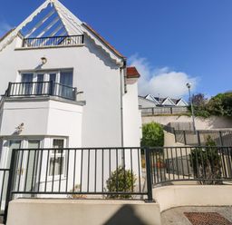 A white house with balconies and black railings under a blue sky at Puffins in Tenby