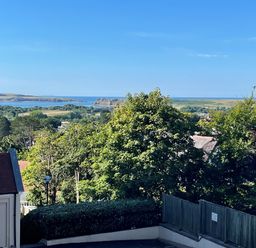 A coastal landscape with trees houses and hills in the background at Puffins in Tenby