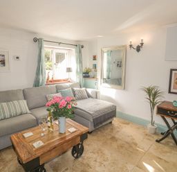 A living room with a gray sectional sofa and a wooden coffee table with flowers and wine glasses at Nightingale Cottage in Lostwithiel