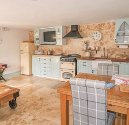 A kitchen with blue cabinets a wooden dining table and checked chairs at Nightingale Cottage in Lostwithiel