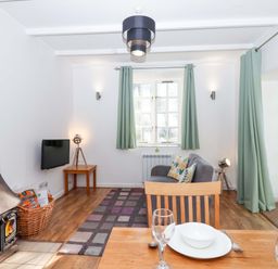 A living room with a wood stove, sofa, and television at Nest Cottage in St Tudy