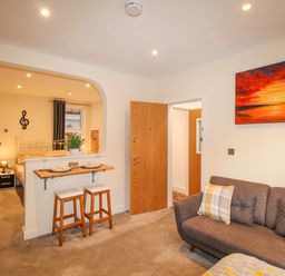 A living room with a grey sofa and bar stools with plates next to an open doorway at Pams House in Weymouth