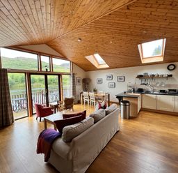 An open living room and kitchen with wooden ceiling and floor large windows and dining table at Ptarmigan Lodge in Glengoulandie near Aberfeldy
