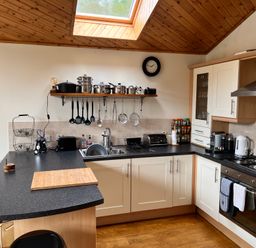 A kitchen with black countertop, white cabinets, stove, sink, hanging utensils, and wooden ceiling at Ptarmigan Lodge in Glengoulandie near Aberfeldy