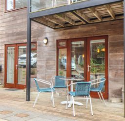 A wooden patio with a round table and four chairs outside double glass doors at Tolcarne in Porthtowan