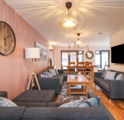 A living room with gray sofas a wooden coffee table wall clock and dining table at Tolcarne in Porthtowan