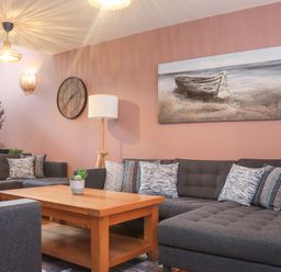 A living room with dark gray sofas patterned cushions wooden coffee table clock plant and a painting of a boat at Tolcarne in Porthtowan