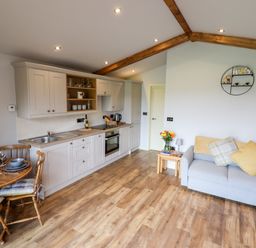 A kitchen and living area with white cabinets wooden dining table and chairs and a light blue sofa at Celyn in Cyffylliog