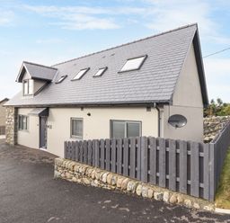 A modern two-story house with slate roof windows and a wooden fence surrounding part of the property at Bryn Hafod in Dyffryn Ardudwy