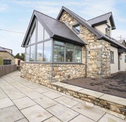 A stone and glass house with a paved pathway and a wooden fence at Bryn Hafod in Dyffryn Ardudwy