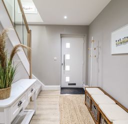 A hallway with a white door a coat rack a bench with cushions and baskets a white table with a plant and a stairway at Bryn Hafod in Dyffryn Ardudwy