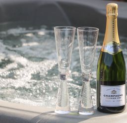 A bottle of champagne and two empty glasses on the edge of a hot tub at Chalet 1 in Sherburn