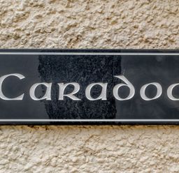 A black rectangular plaque with the word Caradoc on a textured wall at Caradoc Tutshill near Chepstow