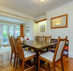 A dining room with a wooden table and chairs next to a bookshelf and a seating area at Caradoc in Tutshill near Chepstow