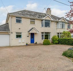 A semi detached house with a blue door a garage and a driveway with bushes and a tree at Caradoc Tutshill near Chepstow