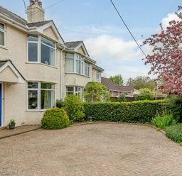 A brick driveway in front of a house with a blue door shrubs and a tree with pink flowers at Caradoc Tutshill near Chepstow
