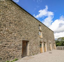 Exterior view of a stone building with wooden doors and windows under a blue sky at Hollowgill Barn in Sedbergh