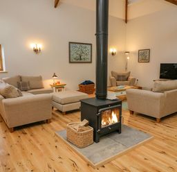 A living room with beige sofas a wood burning stove and a television at Hollowgill Barn in Sedbergh