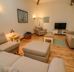 A living room with beige sofas and armchairs wooden floor and a television on a cabinet at Hollowgill Barn Sedbergh