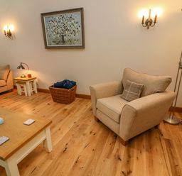 A living room with beige armchair sofa wooden coffee table and a painting on the wall at Hollowgill Barn in Sedbergh