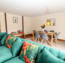 A living room with a green sofa and colorful pillows next to a wooden dining table with grey chairs at Wheal Prosper@The West Dry in St Austell