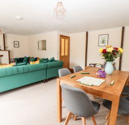 A living room with green sofas a wooden dining table with chairs and a vase of flowers a Scrabble game on the table and a fireplace at Wheal Prosper@The West Dry in St Austell