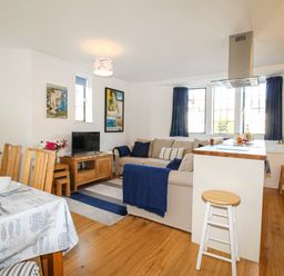 A living and dining area with a sofa a television dining table with chairs and a kitchen island stool at Broadleys Swanage