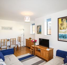 A living room with sofas a dining table with chairs a tv on a wooden stand and wall art at Broadleys in Swanage