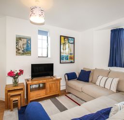 A living room with beige sofas blue cushions a wooden TV stand with a television and nested wooden tables with flowers at Broadleys in Swanage