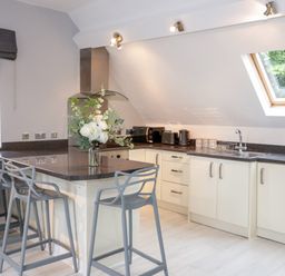 A kitchen with a countertop island with chairs and appliances under a slanted ceiling with skylight at 1 Old Kingdom Hall in Amlwch