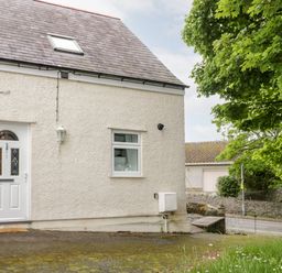 The exterior of a cream colored house with a white door and window near a road and a tree at 1 Old Kingdom Hall in Amlwch