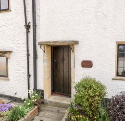 A cottage entrance with a dark wooden door surrounded by plants and flowers at Red Roof in Marsh near Combe St Nicholas