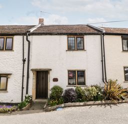 White stone cottages with wooden doors and windows and garden beds in front at Red Roof Marsh near Combe St Nicholas